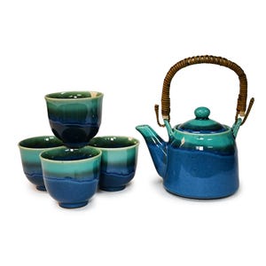 May include: A ceramic tea set consisting of a teapot with a woven brown handle and four matching cups. Each piece features a gradient glaze transitioning from a light turquoise at the top to a deep royal blue at the base with a smooth finish.
