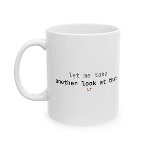 May include: A white ceramic mug featuring the text "let me take another look at that" printed in black and gray lettering, with a small orange curved arrow icon positioned directly below the text on the front of the smooth, cylindrical vessel.