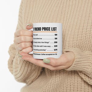 May include: A white ceramic mug featuring black text that reads IT FRIEND PRICE LIST followed by a list of services and prices, including I'll take a look $60, You hover behind me $95, You already tried a few things $150, A YouTube video said it was easy $210, It was working yesterday $275, and No family discount. Coffee accepted as a tip.
