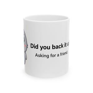 May include: A white ceramic mug featuring a cartoon grey creature with large eyes and pink cheeks on the left side. The text printed in black on the side of the mug reads, Did you back it up? Asking for a friend. The mug has a cylindrical shape.