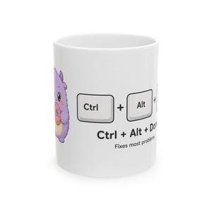May include: A white ceramic mug featuring a purple cartoon monster holding a pink doughnut. The design includes keyboard key graphics labelled Ctrl and Alt, followed by the text Ctrl + Alt + Donut and the phrase Fixes most problems.
