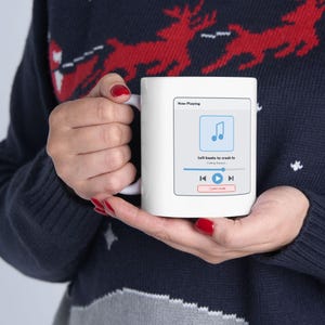 Peut inclure: Un mug en céramique blanche orné d'un graphique d'interface de lecteur de musique numérique. L'écran affiche le texte Now Playing, Lofi beats to crash to et Coding Session, ainsi qu'une icône de note de musique bleue et des commandes.