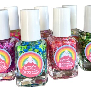 May include: Set of six small bottles of nail polish with glitter. Each bottle has a rainbow and mountain design with the text "Candy Lacquer". The colors of the nail polish are pink, green, blue, red, and green.