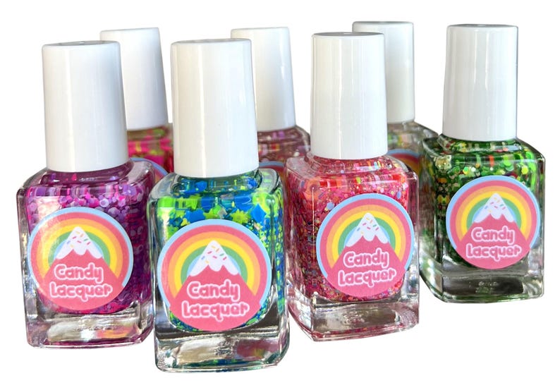 May include: Set of six small bottles of nail polish with glitter. Each bottle has a rainbow and mountain design with the text "Candy Lacquer". The colors of the nail polish are pink, green, blue, red, and green.