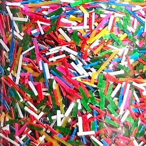 May include: A close-up of a container filled with colorful, thin, plastic strips. The strips are in various colors, including red, blue, green, yellow, and white.
