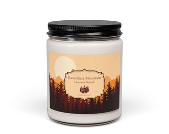 Könnte beinhalten: Eine weiße Kerze in einem klaren Glasgefäß mit schwarzem Metalldeckel. Das Etikett zeigt einen Sonnenuntergang über einem Wald mit dem Text Ravenhart Mountain, Christmas Warmth und einem kleinen Hüttensymbol.