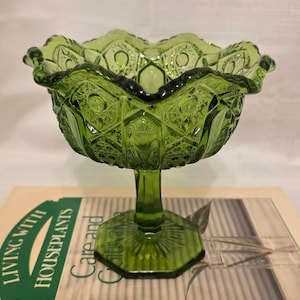 May include: A green glass pedestal bowl with a scalloped rim. The bowl has a detailed, textured pattern and sits on a hexagonal base. The bowl is approximately 8 inches tall.