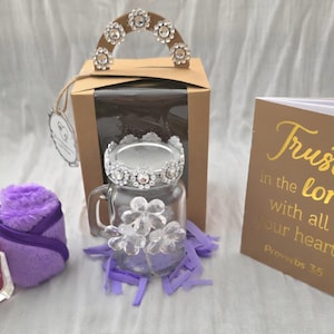 Op de afbeelding: Een geschenkset met een beige doos met een strass handvat, een glazen pot met een strass deksel en bloemversieringen, een flesje Bebe nagellak, een paars pluche item en een beige kaart met de tekst Trust in the lord.