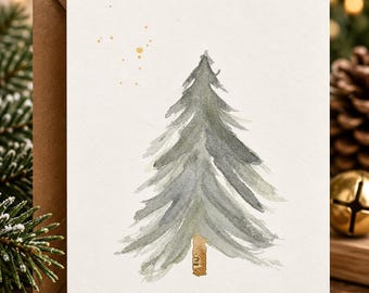 May include: A white greeting card featuring a watercolor illustration of a green pine tree with a brown trunk. Above the tree are small, scattered gold paint splatters. The card is paired with a brown kraft paper envelope.