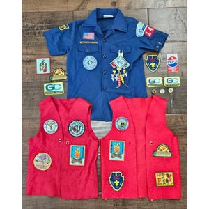 May include: A blue short-sleeved button-down shirt with Boy Scouts of America patches and two red felt vests adorned with various embroidered scouting patches, including camp, council, and activity emblems, plus three small metal pins.
