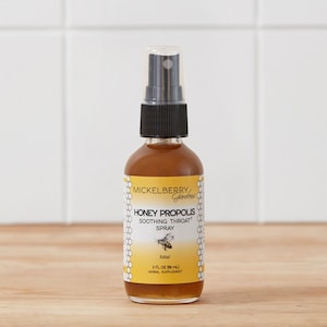 May include: A clear glass bottle with a black spray nozzle, labeled "MICKELBERRY Gardens HONEY PROPOLIS SOOTHING THROAT SPRAY RAW 2 FL OZ (50 mL) HERBAL SUPPLEMENT".