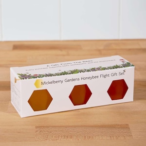 May include: A white box with a floral design and the text "A Gift From The Bees" and "Mickelberry Gardens Honeybee Flight Gift Set". The box contains three honeycombs, two are orange and one is yellow.