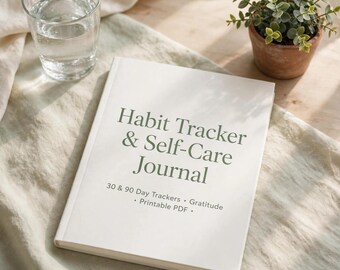 Op de afbeelding: Een wit dagboek met de tekst Habit Tracker & Self-Care Journal, 30 & 90 Day Trackers, Gratitude en Printable PDF in donkergroene letters op de kaft. Het dagboek ligt op een lichtgekleurde stoffen ondergrond.