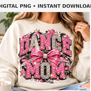 Può includere: Una felpa color crema con un design grafico che riporta la scritta DANCE MOM in lettere stile glitter rosa e argento. Il design include un grande fiocco rosa, nastri neri e varie forme di stelle, il tutto accentuato da dettagli scintillanti.