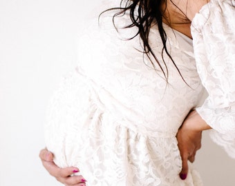 May include: A pregnant woman wearing a white lace off-the-shoulder dress.