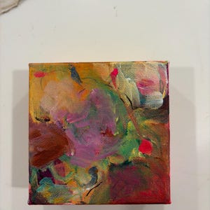 Op de afbeelding: Een klein vierkant schilderij op canvas met een abstracte compositie van gelaagde penseelstreken in levendige tinten magenta, dieprood, mosterdgeel, bosgroen en witte accenten, wat zorgt voor een getextureerd en veelkleurig oppervlak.