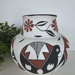 May include: A rounded ceramic vase with a matte white finish, featuring hand-painted black and terracotta red geometric patterns and stylized bird motifs. The neck is decorated with a floral vine design in black and red.