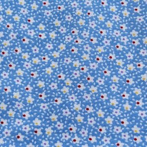 May include: Close-up of a light blue fabric with a repeating floral pattern. Tiny white flowers with yellow centers and red and purple dots are scattered across the surface, creating a delicate and charming design.