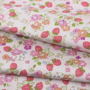 May include: Close-up of a white fabric with a repeating pattern of pink strawberries and small flowers in shades of pink, orange, and purple. The fabric has a soft, slightly wrinkled appearance, suggesting it is likely cotton or a similar material.