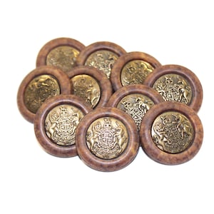 May include: A collection of ten round buttons with a brown wooden frame and a gold-colored emblem in the center. The emblem features a coat of arms design. The buttons are arranged on a white background.