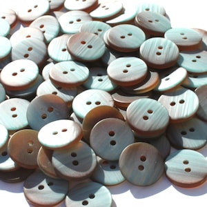 May include: A pile of round buttons with two holes each. The buttons have a two-tone color scheme, with a light teal and brown swirl pattern. The buttons are scattered on a white surface.