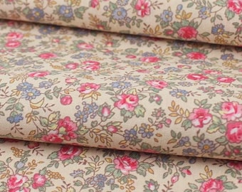 May include: Close-up of a floral fabric with a cream-colored background. The fabric is covered in a pattern of small pink roses, blue flowers, and green leaves. The fabric is folded over itself.