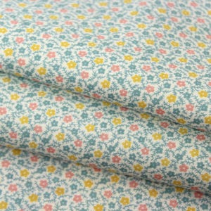 May include: Close-up of a fabric with a floral pattern. The fabric has a pale blue background with small yellow and pink flowers and green stems. The fabric is folded over, showing the pattern in detail.
