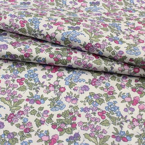 May include: A white fabric featuring a dense, repeating floral pattern with small pink, purple, and light blue flowers interspersed with green leaves and stems. The textile has a soft, folded texture, showcasing the intricate botanical print throughout.