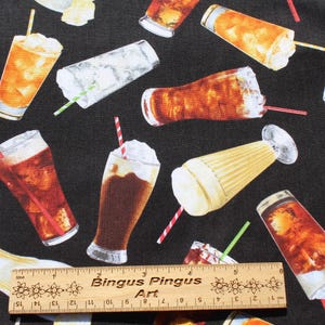 May include: Black fabric featuring a pattern of refreshing drinks, such as iced tea, fizzy drinks, and milkshakes. The drinks are in glasses and bottles, with straws. A wooden ruler is at the bottom.