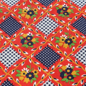 May include: Close-up of a red fabric with a repeating pattern. The pattern features navy blue polka dot and checkered squares, yellow and navy blue flowers, and white leaves. The design is arranged in a grid with yellow vines.