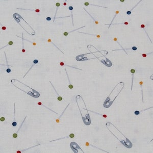 May include: A white fabric with a repeating pattern of safety pins and colorful beads. The safety pins are silver and the beads are red, blue, green, and yellow.