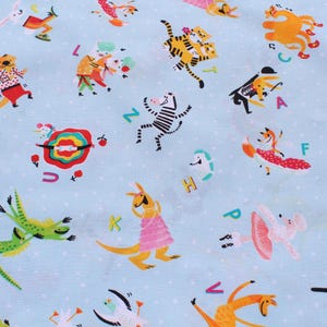 May include: Light blue fabric with a repeating pattern of cartoon animals, letters, and white polka dots. The animals include a zebra, fox, kangaroo, and others, all in colorful outfits. Letters of the alphabet are scattered throughout the design.