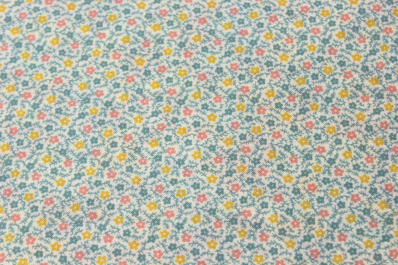 May include: A close-up of a fabric with a repeating floral pattern. The design features small pink and yellow flowers with green stems and leaves on a pale blue background. The fabric has a delicate, textured appearance.