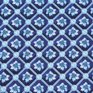 May include: Close-up of a fabric with a repeating pattern of light blue floral designs set within a grid of light blue lines and circles, against a dark blue background. The floral pattern is detailed and symmetrical.