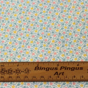 May include: Pale blue fabric covered in small yellow and pink flowers. A wooden ruler, marked in inches, with the text "Bingus Pingus Art" is placed across the bottom of the fabric.