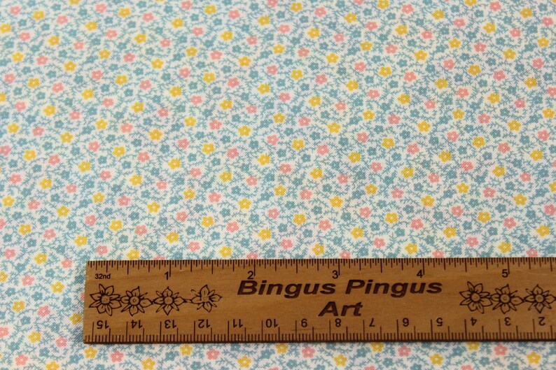 May include: Pale blue fabric covered in small yellow and pink flowers. A wooden ruler, marked in inches, with the text "Bingus Pingus Art" is placed across the bottom of the fabric.