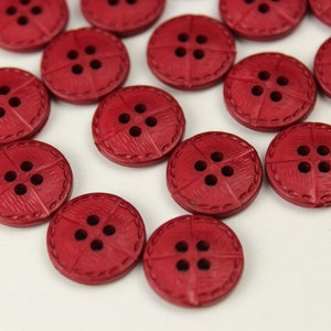 May include: A collection of red buttons with four holes each. The buttons have a textured surface and a decorative stitched edge.