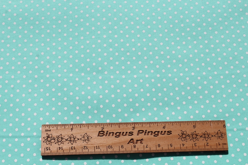 May include: A turquoise fabric with a white polka dot pattern. A wooden ruler with the text "Bingus Pingus Art" is placed on the fabric.