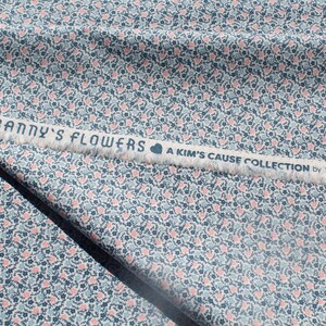 May include: Fabric with a floral pattern in blue, pink, and white. The fabric features a repeating design of small flowers and hearts. A white strip with the text "FRANNY'S FLOWERS A KIM'S CAUSE COLLECTION by MAYWOOD" is visible.
