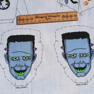 May include: A light blue fabric with two cartoon Frankenstein faces, each with black hair, green eyes, and a stitched mouth. The fabric also features a ruler with the text "Bingus Pingus Art" and Halloween-themed illustrations.