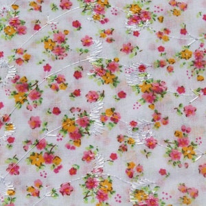 May include: White fabric with a delicate floral pattern featuring pink and yellow flowers. The fabric has a subtle sheen and a delicate, embroidered design.