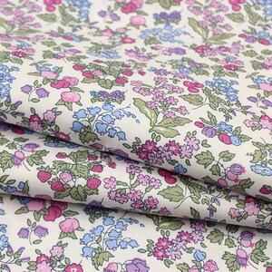 May include: A fabric featuring a repeating pattern of small pink, blue, and purple flowers interspersed with green leaves and red strawberries on an off-white background. The textile is folded to show the intricate botanical print and texture.