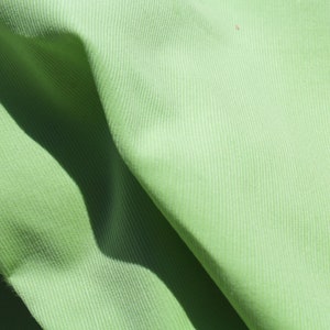 May include: A close-up of a light green fabric with a ribbed texture. The fabric is folded and has a slight sheen.