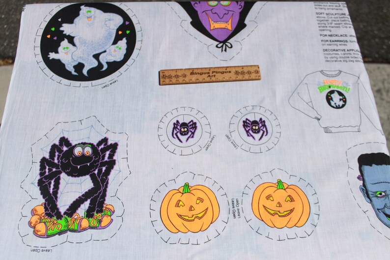 May include: A light blue Halloween-themed fabric featuring various cut-out designs. Includes a ghost, spider, pumpkin, and vampire. The fabric also has a ruler with the text "Bingus Pingus Art".