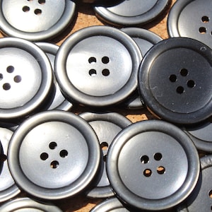 May include: A close-up of a pile of black and silver buttons. The buttons are round and have four holes each.