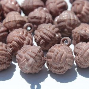 May include: A group of 14 brown plastic buttons with a woven design and a loop on top. The buttons are arranged in a random pattern on a white surface.
