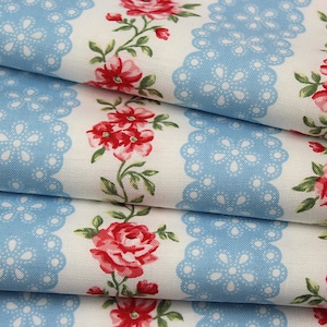 May include: A folded fabric featuring a white background with vertical stripes of light blue scalloped lace patterns and repeating floral motifs of red roses with green leaves and stems arranged in a continuous vertical line pattern.