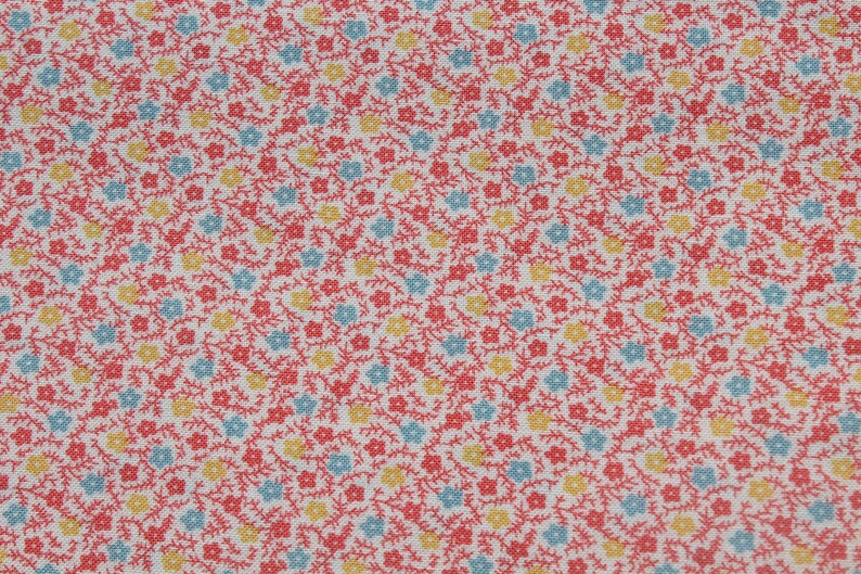 May include: Close-up of a fabric with a repeating floral pattern. The design features small red, yellow, and light blue flowers with green stems on a white background. The fabric has a textured appearance.
