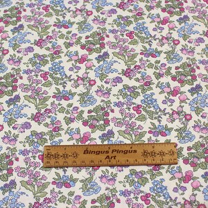 May include: A fabric with a repeating floral pattern featuring small pink, purple, and blue flowers with green leaves on a cream background. A wooden ruler labeled Bingus Pingus Art is placed across the fabric, showing a length of 6 inches.