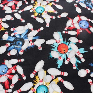 以下が含まれることがあります： 黒色の生地に、ボーリングのピンとボールの繰り返し模様。ピンは白地に赤いストライプ、ボールは赤、青、ターコイズ色。背景は黒色です。